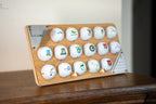 Un support 16 balles avec plaque grave en couleur pose sur n meuble en bois avec ses 2 tees