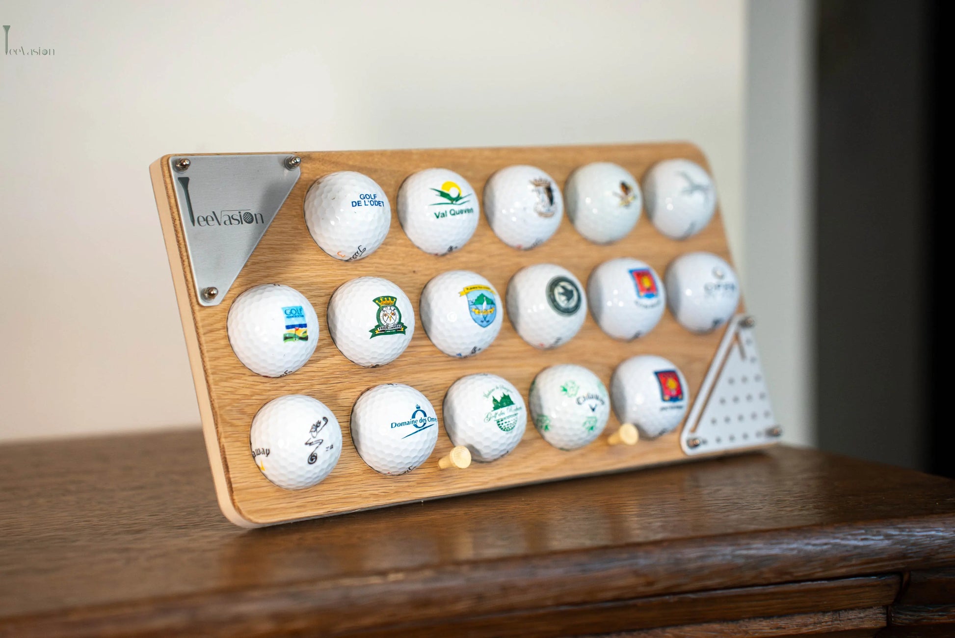 Un support 16 balles avec plaque grave en couleur pose sur n meuble en bois avec ses 2 tees