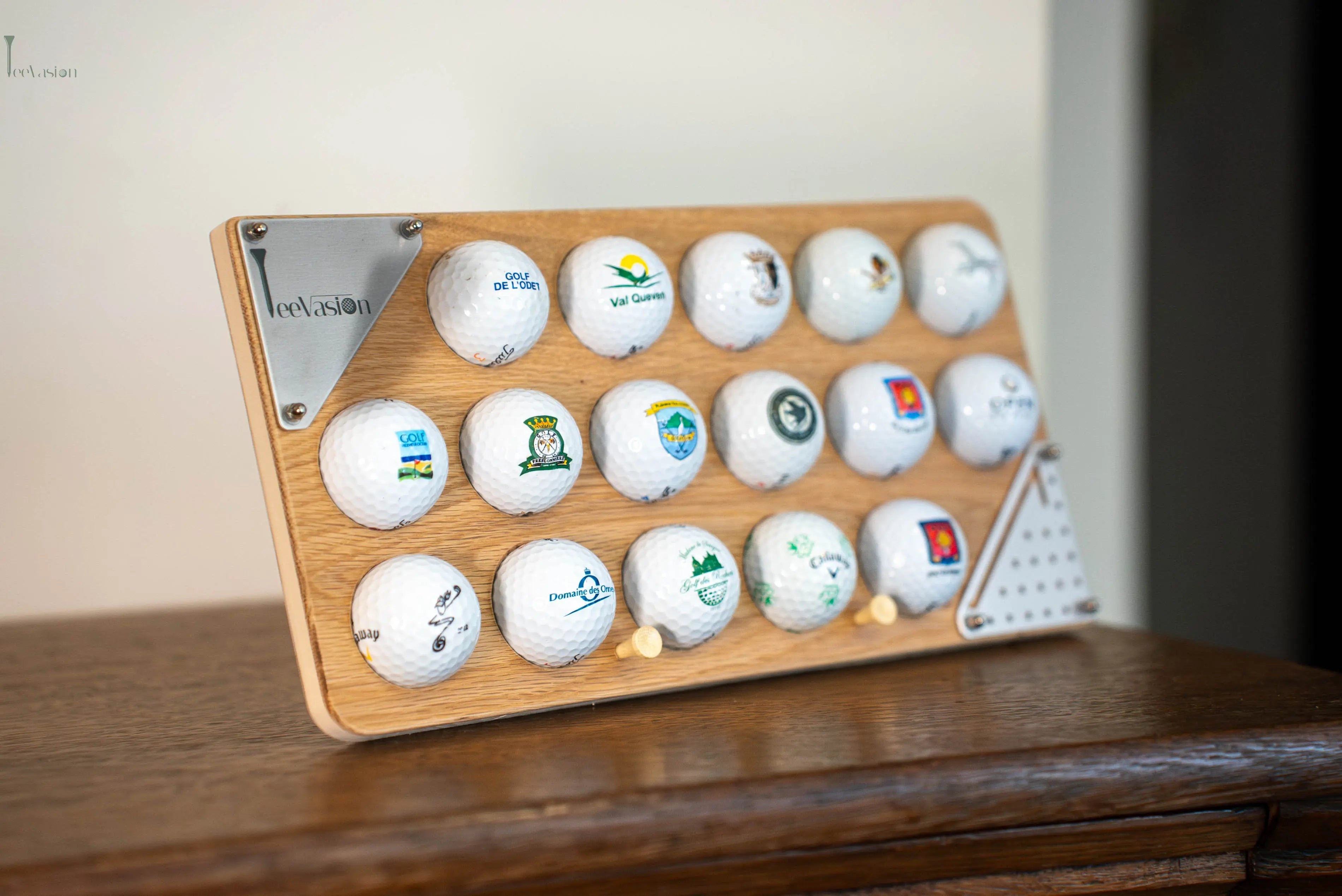 Un support 16 balles avec plaque grave en couleur pose sur n meuble en bois avec ses 2 tees