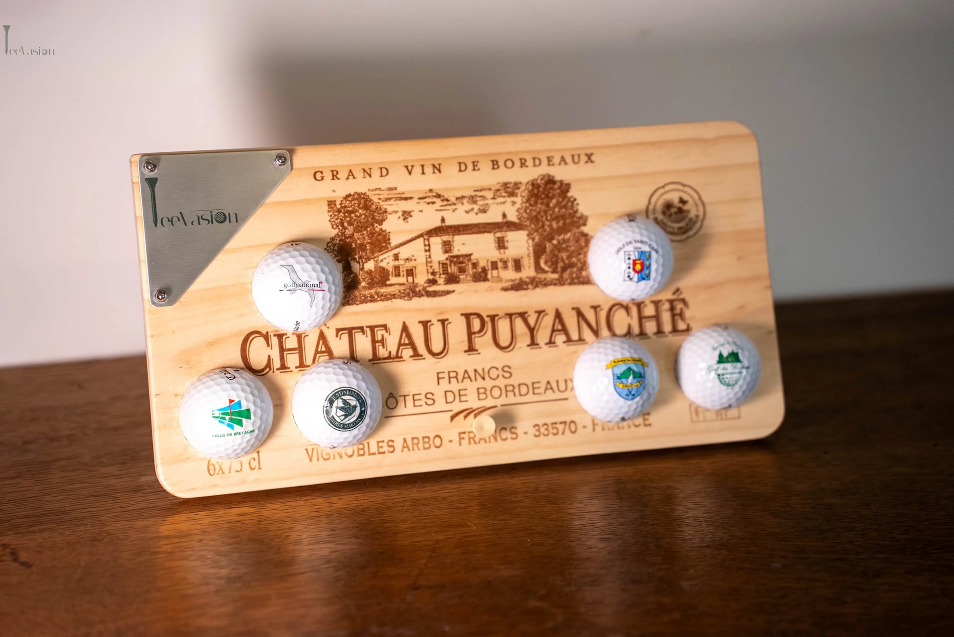 Un support 6 balles sur caisse de vin avec plaque gravure couleur pose sur son tee sur un meuble en bois