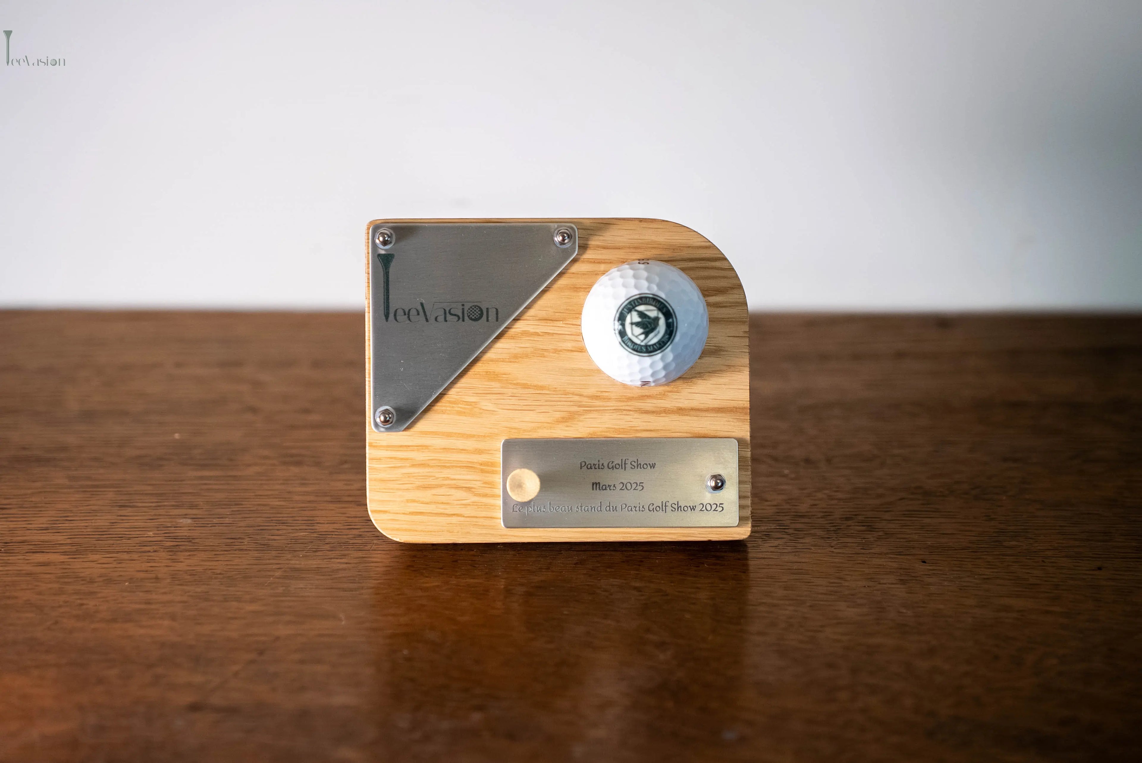 Un trophee 1 balle avec plaque gravure couleur  et sa seconde plaque a l'effigie de la competition pose sur un meuble en bois avec son tee 
